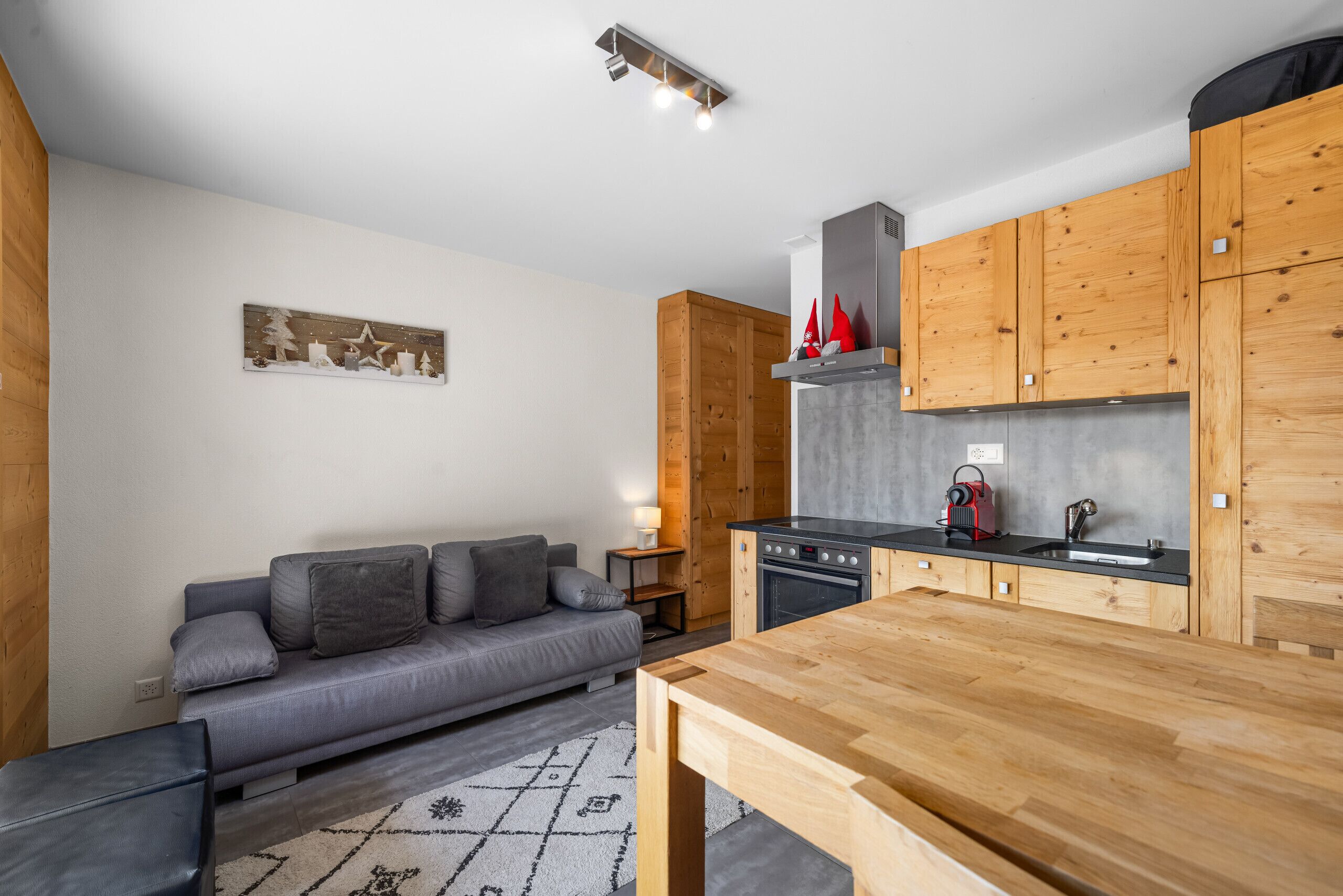 A modern kitchen with wooden cabinets, a grey sofa, and a dining table.