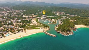 Luftaufnahme einer Küstenlandschaft mit einem Yachthafen, einem Strand und einem dichten Waldgebiet.