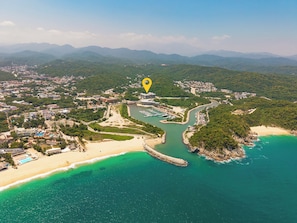 An aerial view of a coastal area with a marina, a beach, and a dense forested area. - Chic 2BR | Beach, Town & Elevated Views (Huatulco)