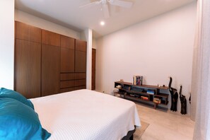 Un dormitorio con cama, armario de madera y un mueble bajo para la televisión con libros y objetos decorativos.