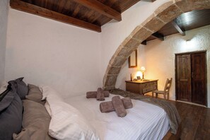 A bedroom with a bed, pillows, a wooden nightstand, a chair, a desk, a lamp, and a door. - Serenity Cave Villa, Traditional Villas Askyfou (Crete)