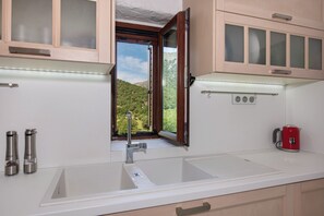 A kitchen with a large window, a sink, and a red kettle. - Serenity Cave Villa, Traditional Villas Askyfou (Crete)