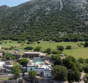 A rural setting with a stone building, a swimming pool, and a lush green landscape. - Serenity Cave Villa, Traditional Villas Askyfou (Crete)