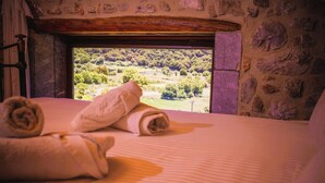 A bed with rolled towels and a view of a green landscape through a window. - Villa Askyfou, Traditional Villas Askyfou (Crete)