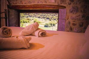 Ein Bett mit zusammengerollten Handtüchern und Blick auf eine grüne Landschaft durch ein Fenster.