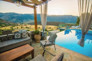A poolside area with a view of mountains, a wooden pergola, a seating area with cushions, and a stone table. - Villa Askyfou, Traditional Villas Askyfou (Crete)