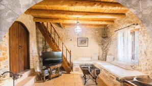 A rustic stone interior with a wooden staircase, a television, a bathtub, and a dining area. - Villa Askyfou, Traditional Villas Askyfou (Crete)