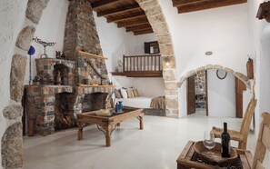 Ein rustikales Interieur mit Kamin aus Stein, Holzmöbeln und einem Rundbogen.
