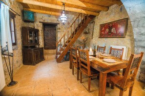 Ein rustikaler Essbereich mit Holztisch, Stühlen, einer Treppe, Steinwänden und einer Chandelüster.