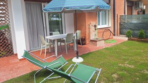 A patio with a table and chairs, a green lawn, and a brick wall. - Beachfront, Modern Flat With Lovely Garden (San Michele al Tagliamento)
