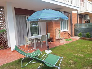 A patio with a table and chairs, a green lawn, and a brick wall. - Beachfront, Modern Flat With Lovely Garden (San Michele al Tagliamento)
