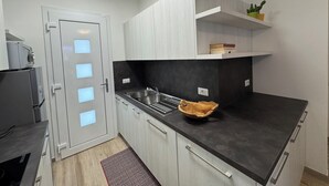 A modern kitchen with a black countertop, white cabinets, a built-in sink, and a wooden bowl. - Beachfront, Modern Flat With Lovely Garden (San Michele al Tagliamento)