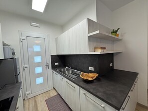 A modern kitchen with a black countertop, white cabinets, a built-in sink, and a wooden bowl. - Beachfront, Modern Flat With Lovely Garden (San Michele al Tagliamento)