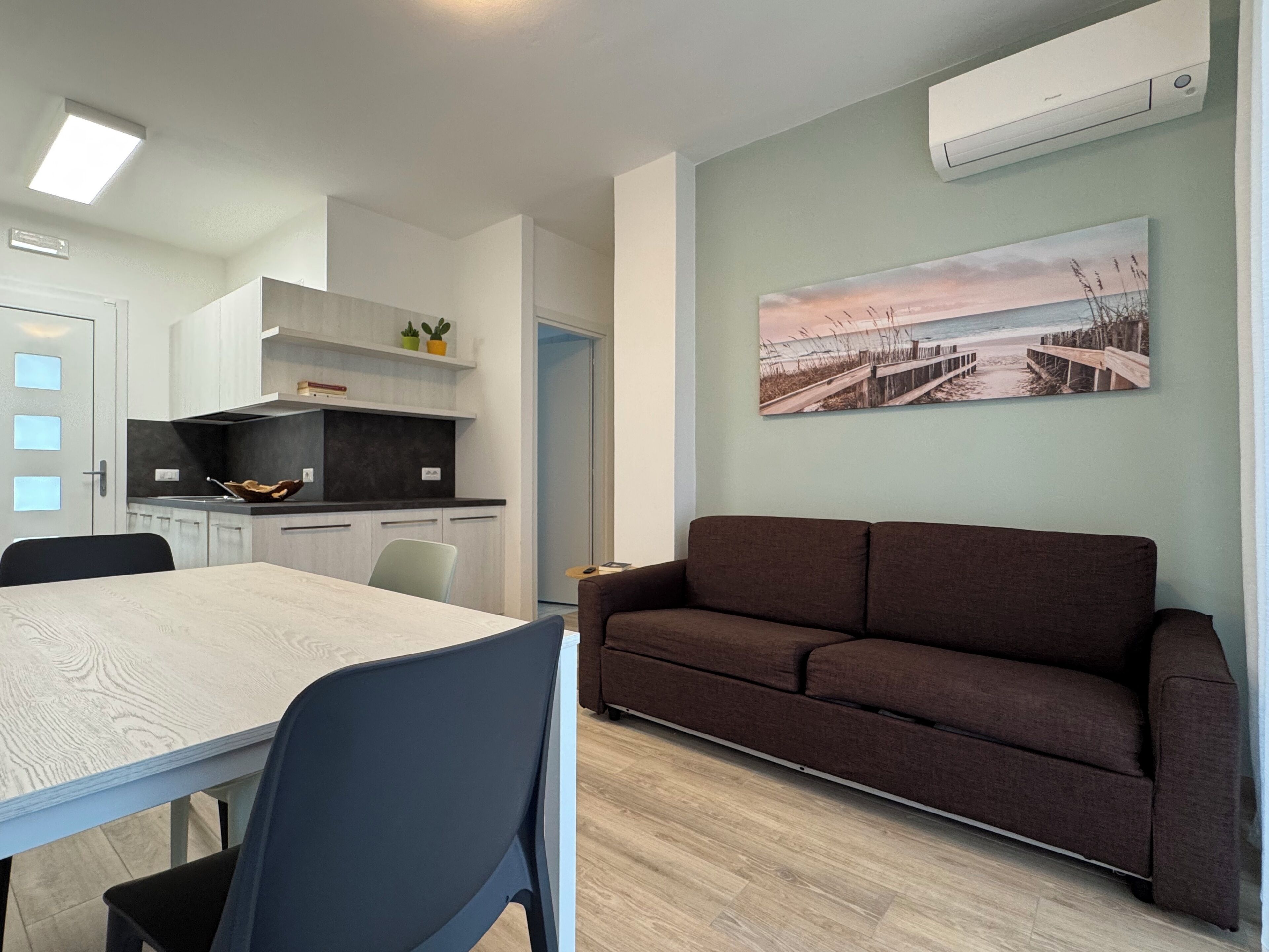 Eine moderne Wohnung mit Essbereich, Küche und Wohnzimmer mit Sofa und Strand-Wandbild.