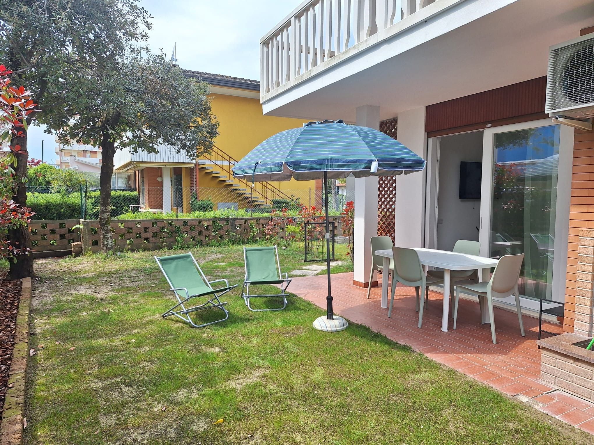 A patio with a table and chairs, a blue umbrella, and a staircase leading to a balcony.