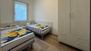 A bedroom with two beds, a wardrobe, a window, and a door. - Beachfront, Modern Flat With Lovely Garden (San Michele al Tagliamento)
