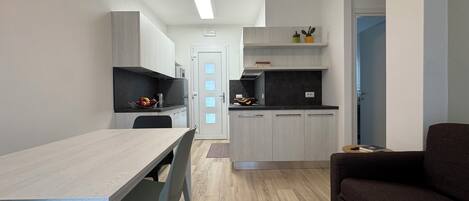 A modern kitchen with a dining area, a sofa, and a door leading to another room.