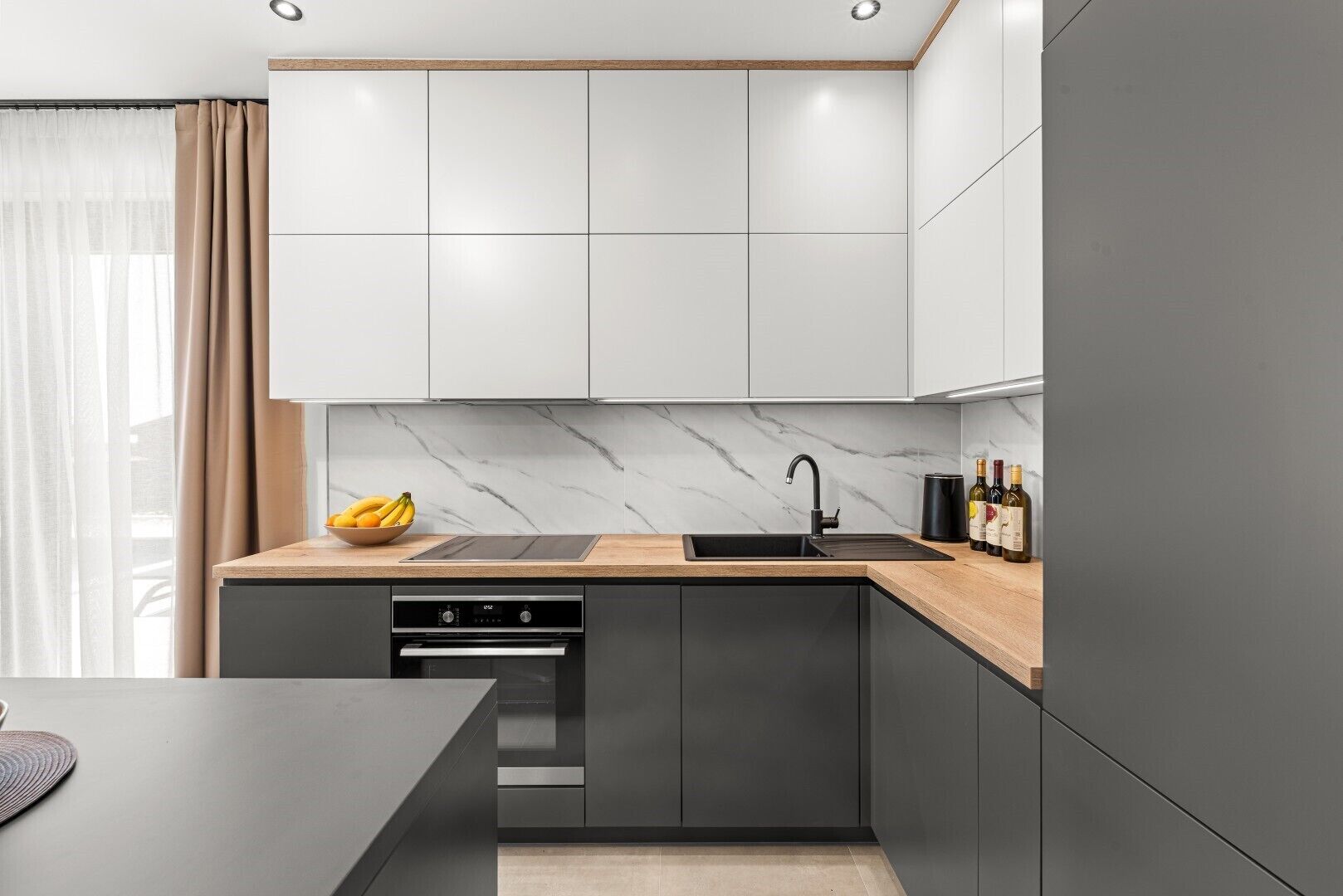 A modern kitchen with a built-in oven, a sink, and a marble backsplash.