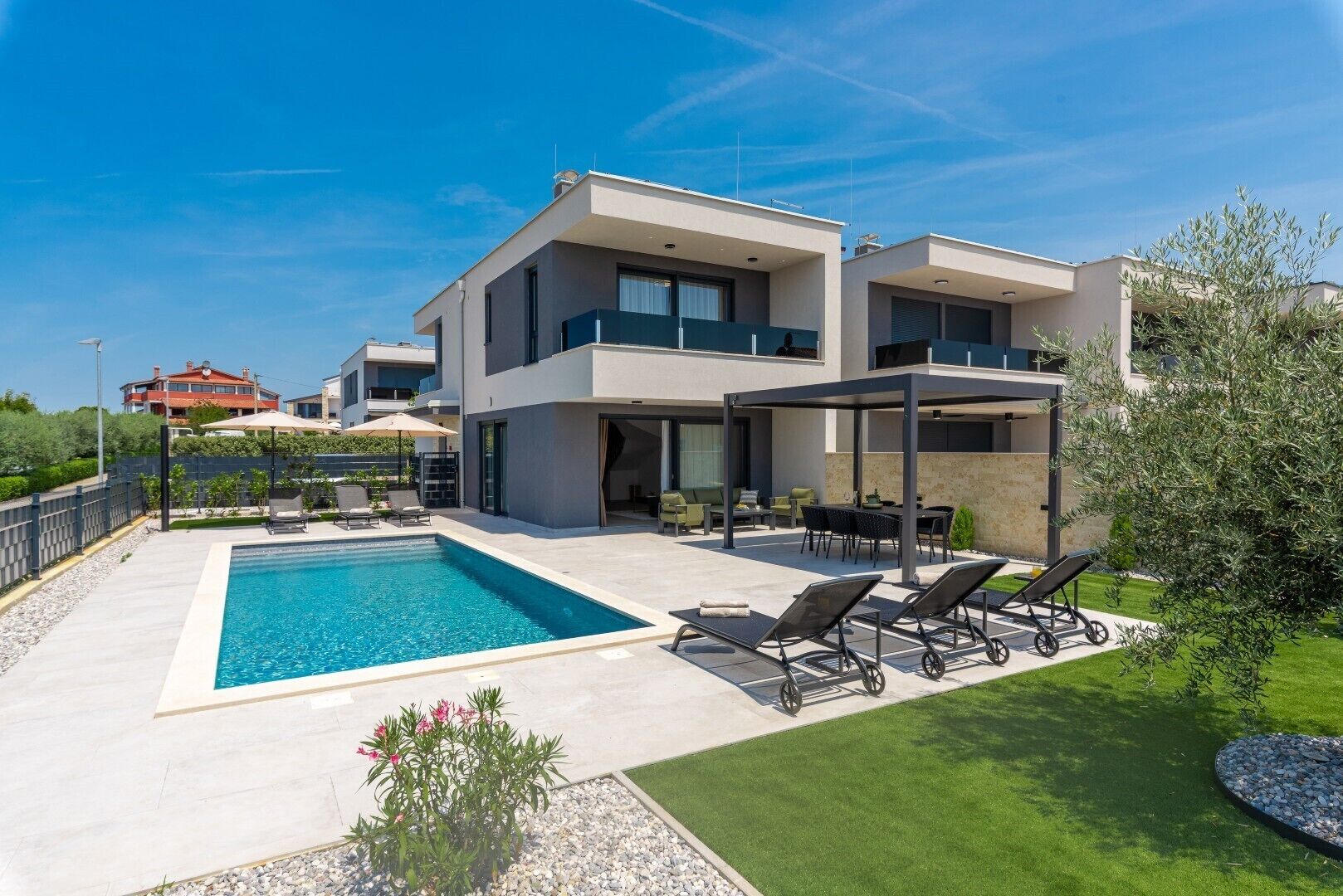 Une maison moderne à deux étages, dotée d’une piscine, d’un espace salon extérieur et d’une pelouse bien entretenue.
