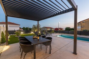 Eine überdachte Terrasse im Freien mit Pool, Esstisch und Stühlen.