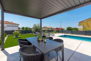 Eine überdachte Terrasse im Freien mit Pool, Sitzgelegenheiten und einem Tisch mit Flasche und Glas.