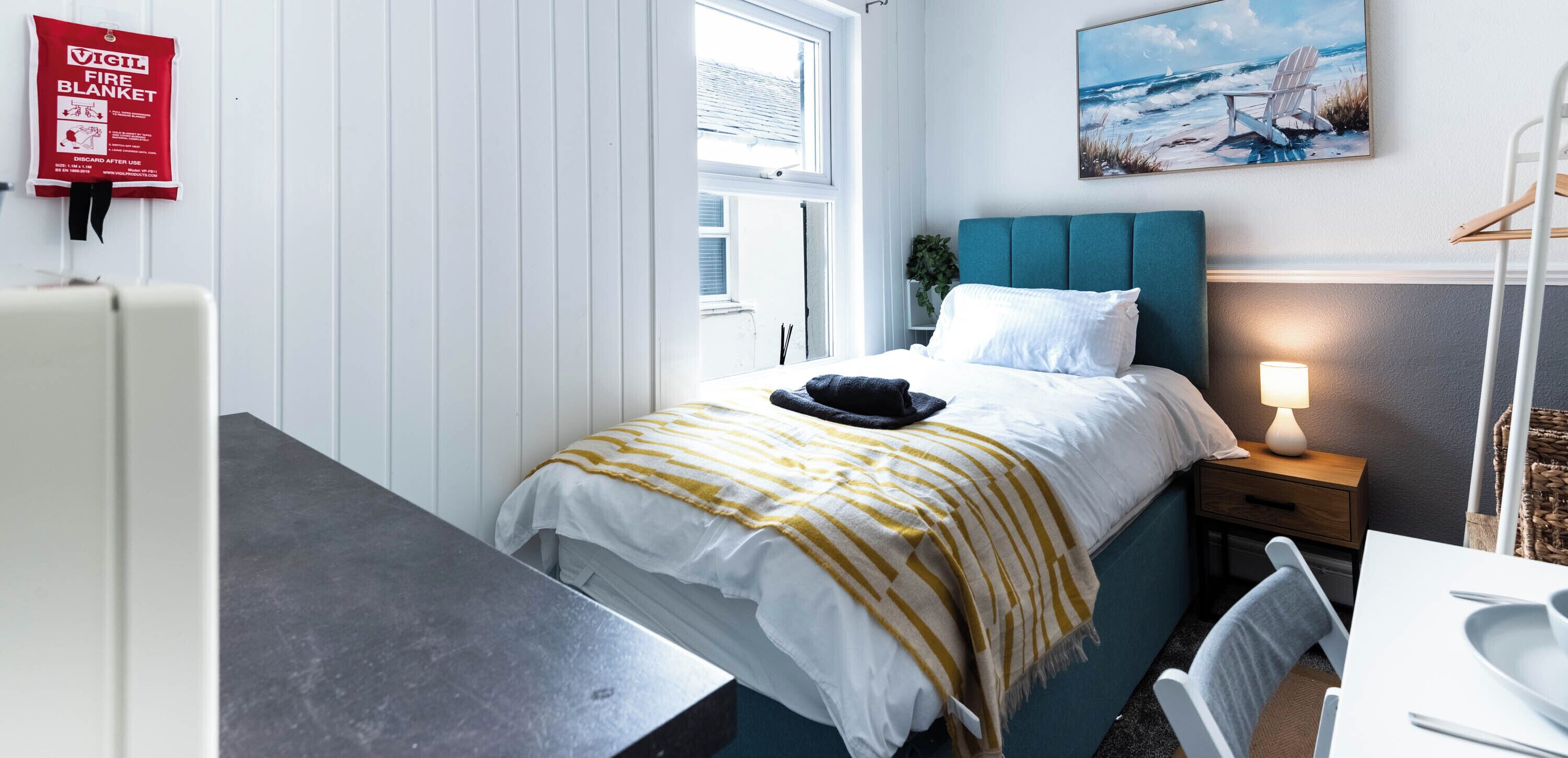A bedroom with a bed, bedside table, lamp, and a painting on the wall.
