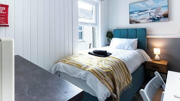 A bedroom with a bed, bedside table, lamp, and a painting on the wall.