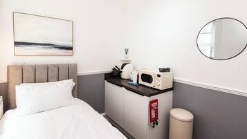 Ett hotellrum med en säng, en mikrovågsugn, ett litet bord med en vattenkokare, en brandfilt och en papperskorg.