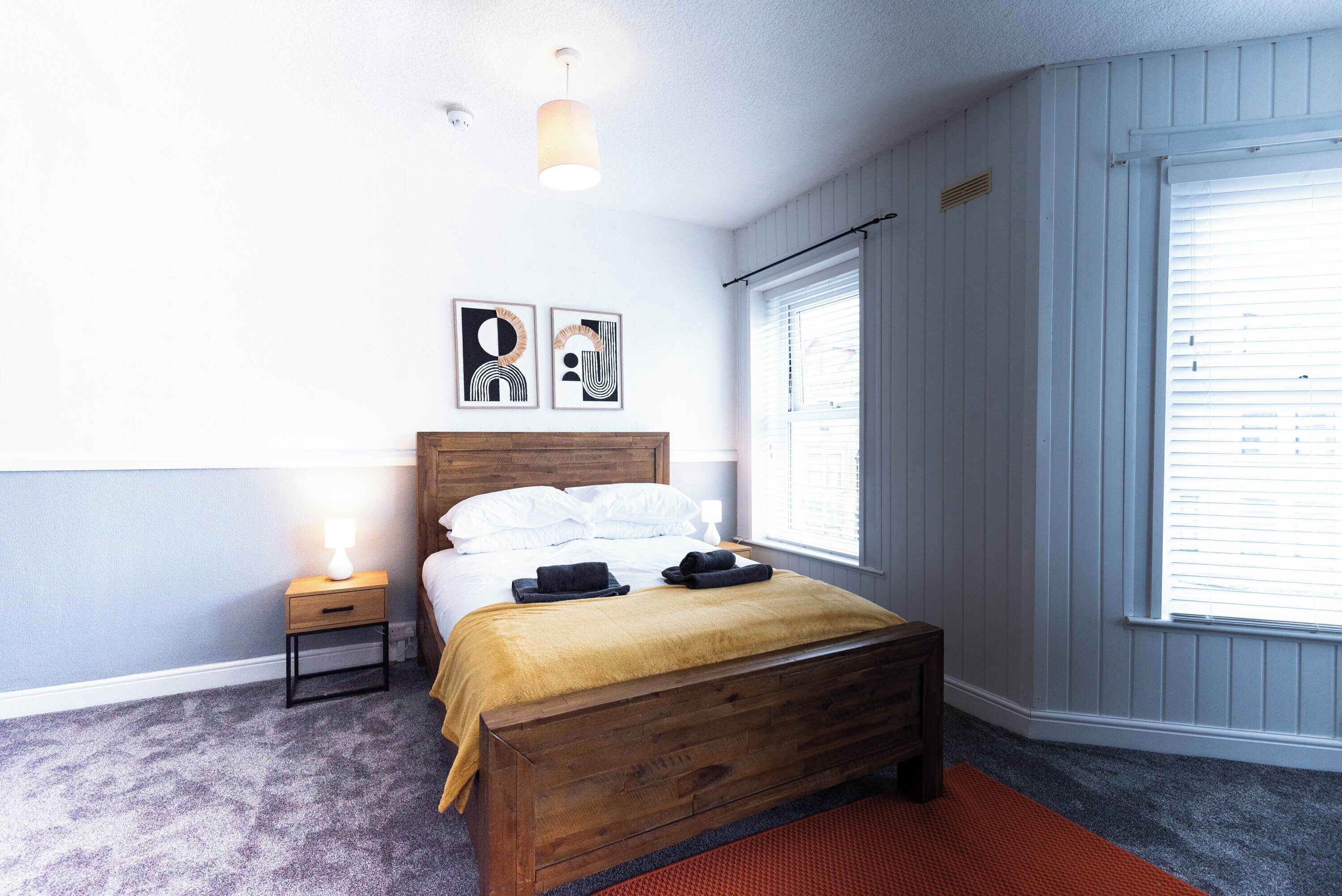 A bedroom with a wooden bed, a nightstand, a lamp, and two wall-mounted artworks.
