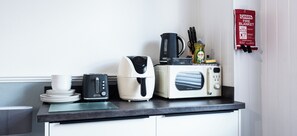 A kitchen counter with a coffee maker, a toaster, a kettle, and a microwave. There is a fire blanket hanging on the wall. - The Bay by Guestz (Morecambe)