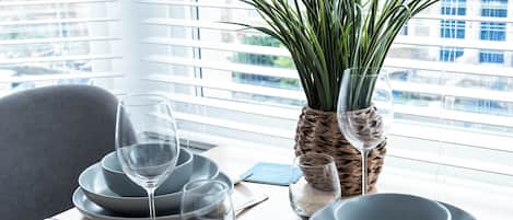 A dining table set with plates, glasses, and cutlery, a potted plant, and a smartphone on the table.