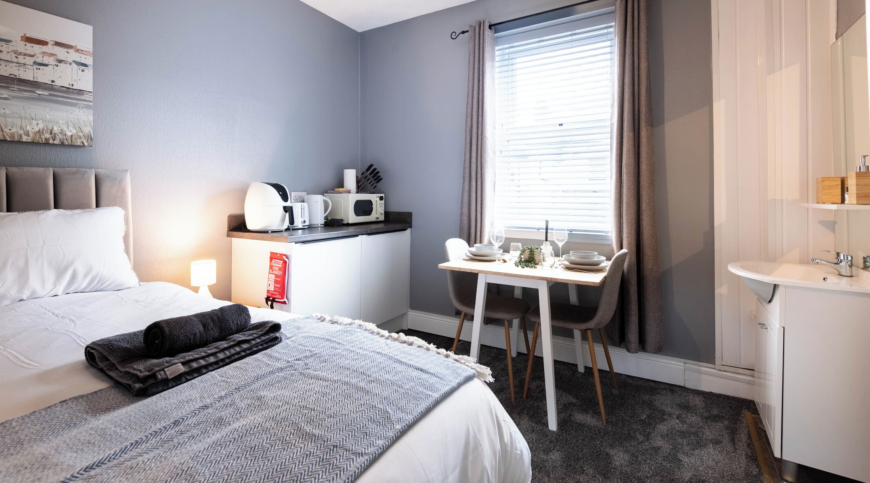 Habitación de hotel con cama, escritorio, microondas, cafetera y ventana con cortinas.