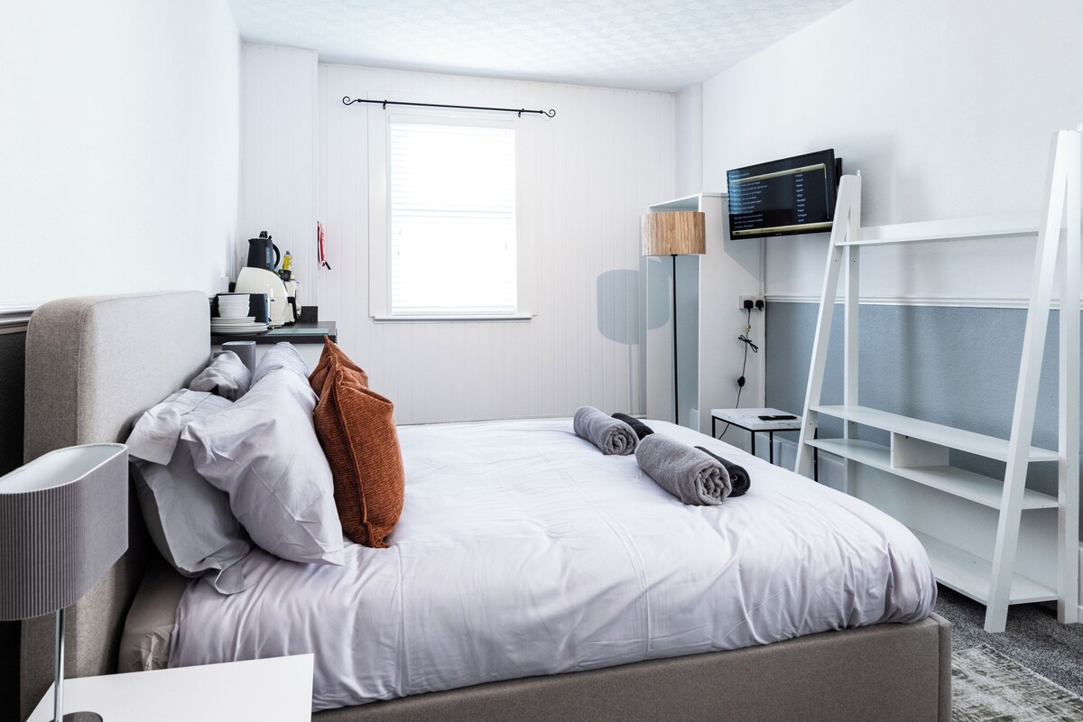 A hotel room with a bed, a desk, a chair, a TV, and a window.