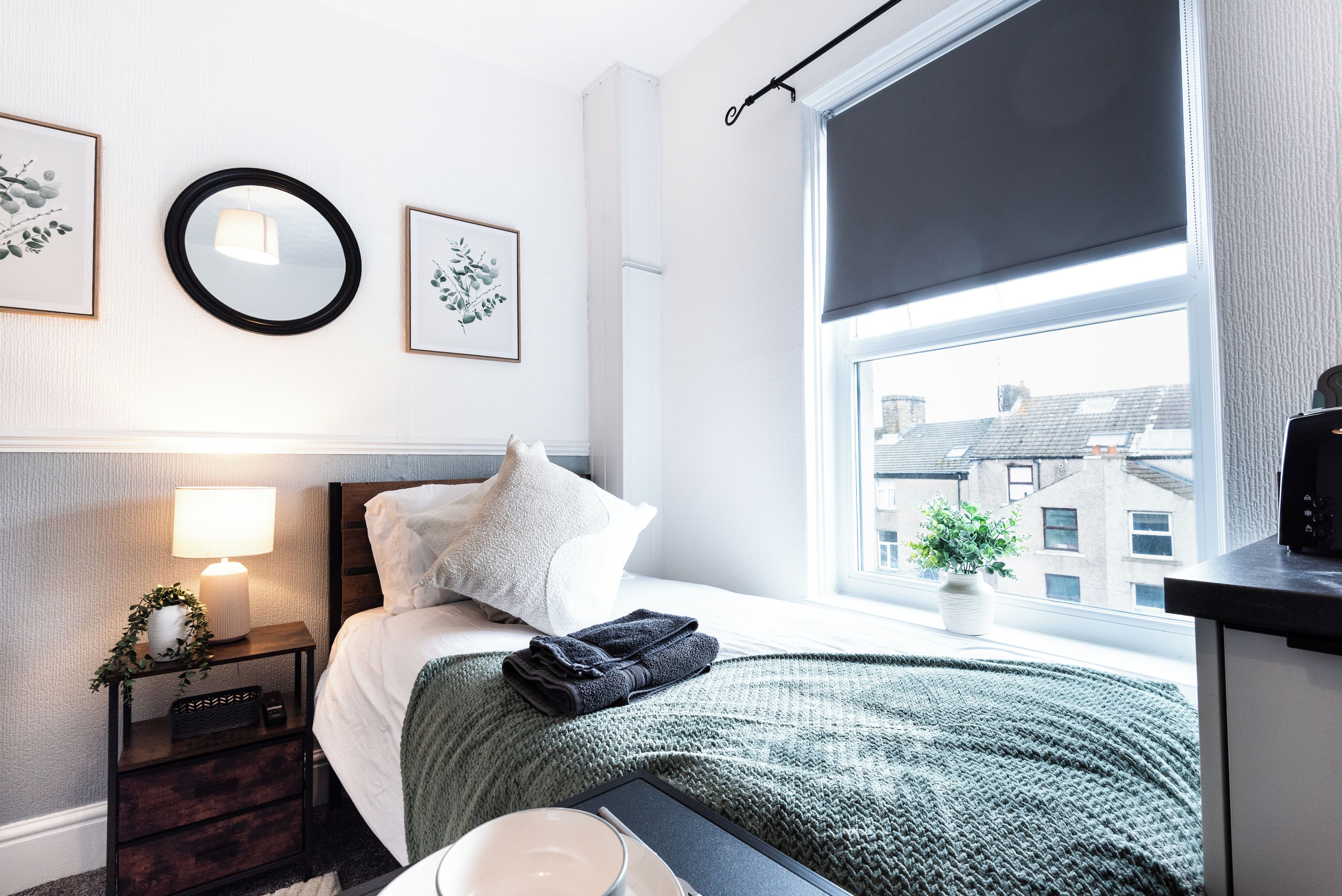 A neatly arranged bedroom with a bed, bedside lamp, and a window with a view of buildings.