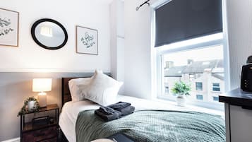 A neatly arranged bedroom with a bed, bedside lamp, and a window with a view of buildings.