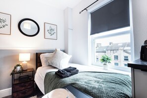 A neatly arranged bedroom with a bed, bedside lamp, and a window with a view of buildings.