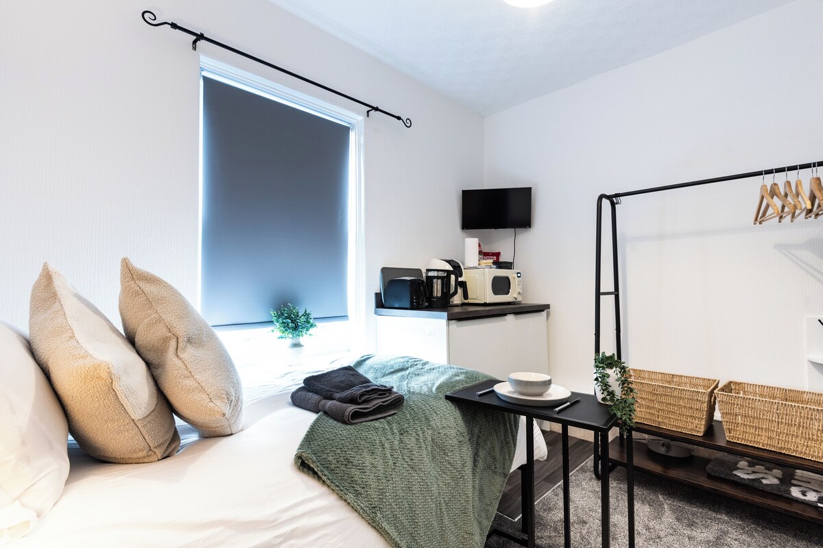 A modern bedroom with a bed, a small table with a bowl and a cup, a TV on a shelf, and a window with a view.