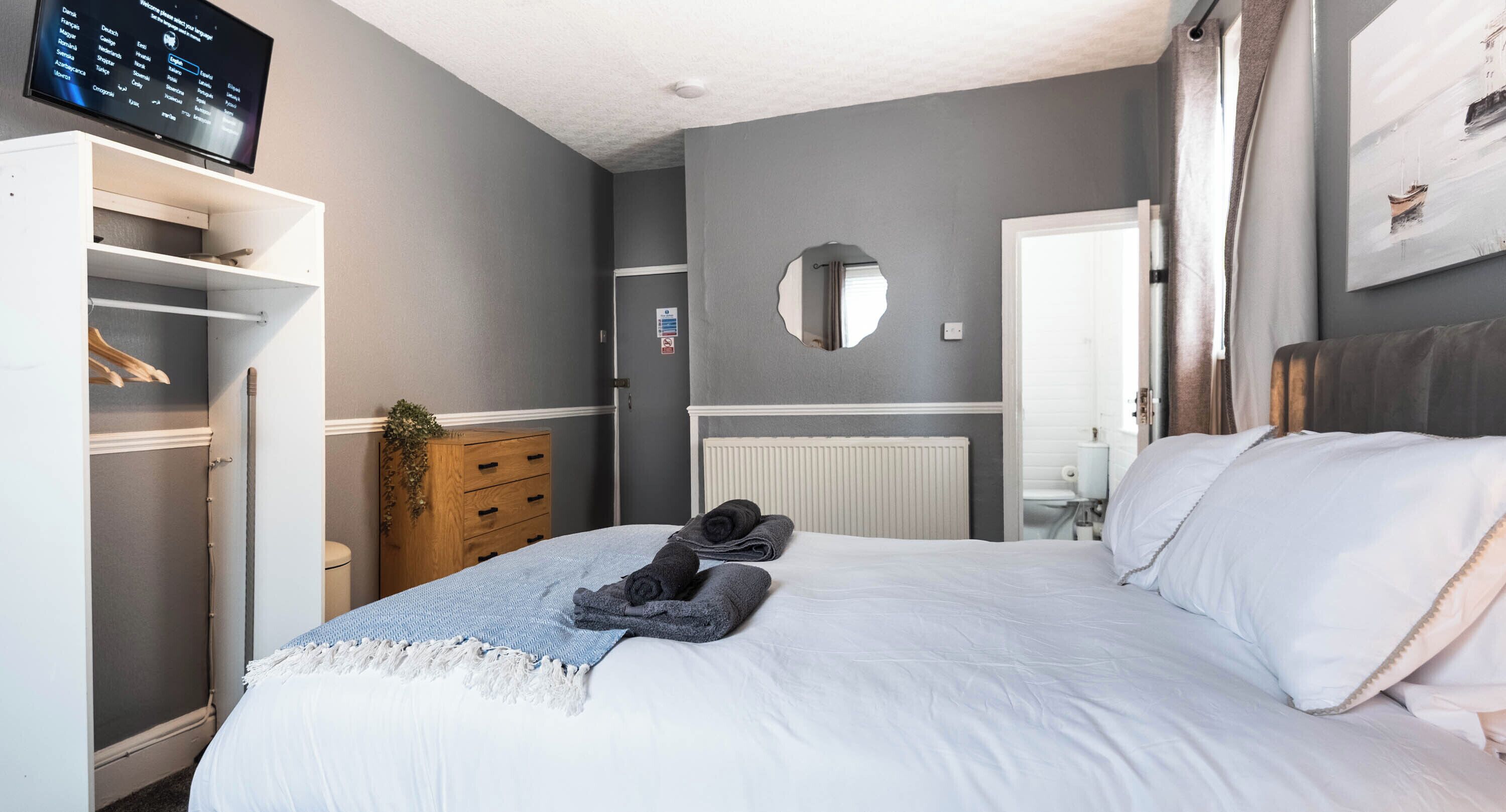 A bedroom with a bed, a TV, a wardrobe, and a mirror.