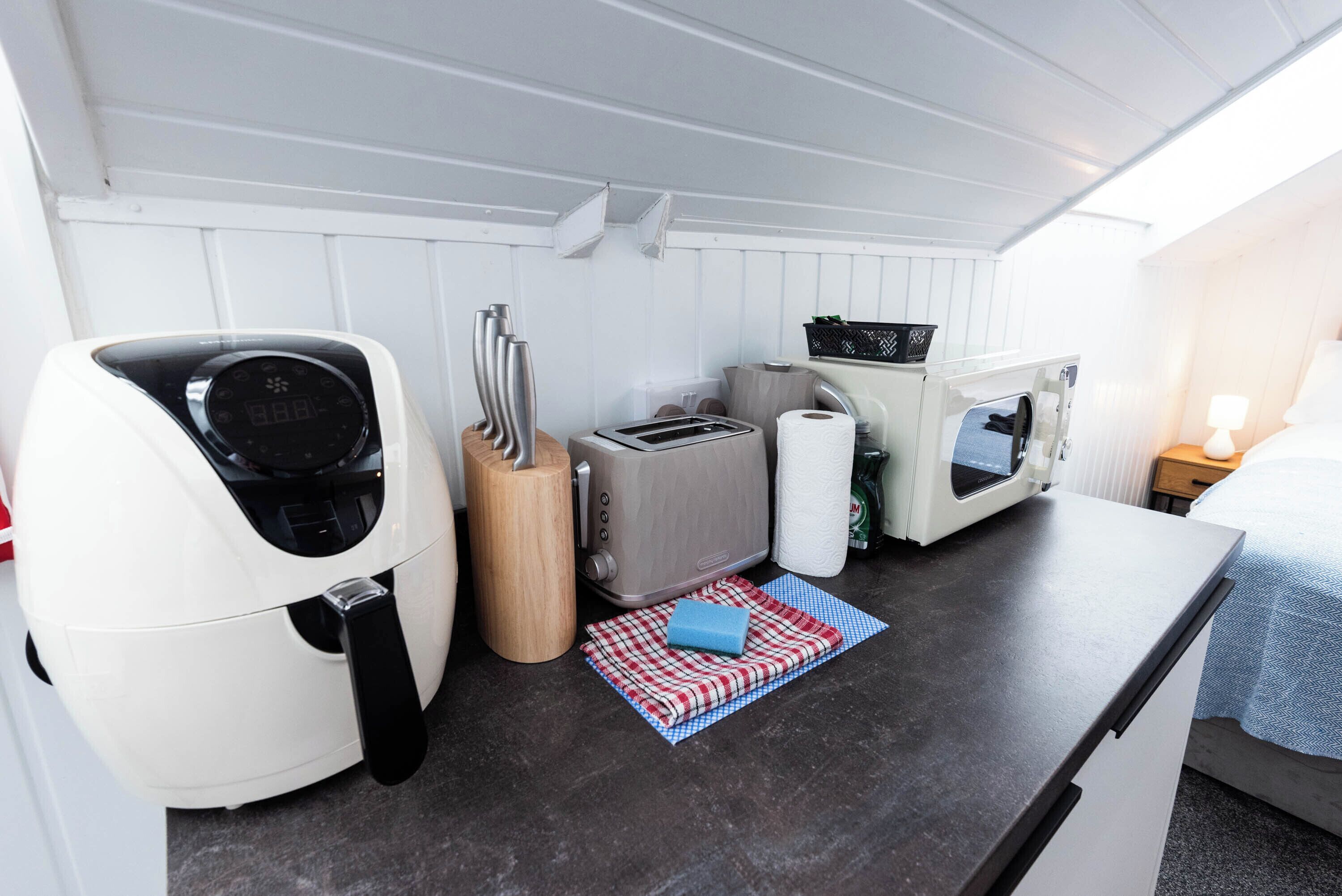 A compact kitchenette with a microwave, toaster, and a small table with a kettle and a basket.