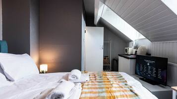 Quarto de hotel com cama, televisão, pequena cozinha e vista para o céu.