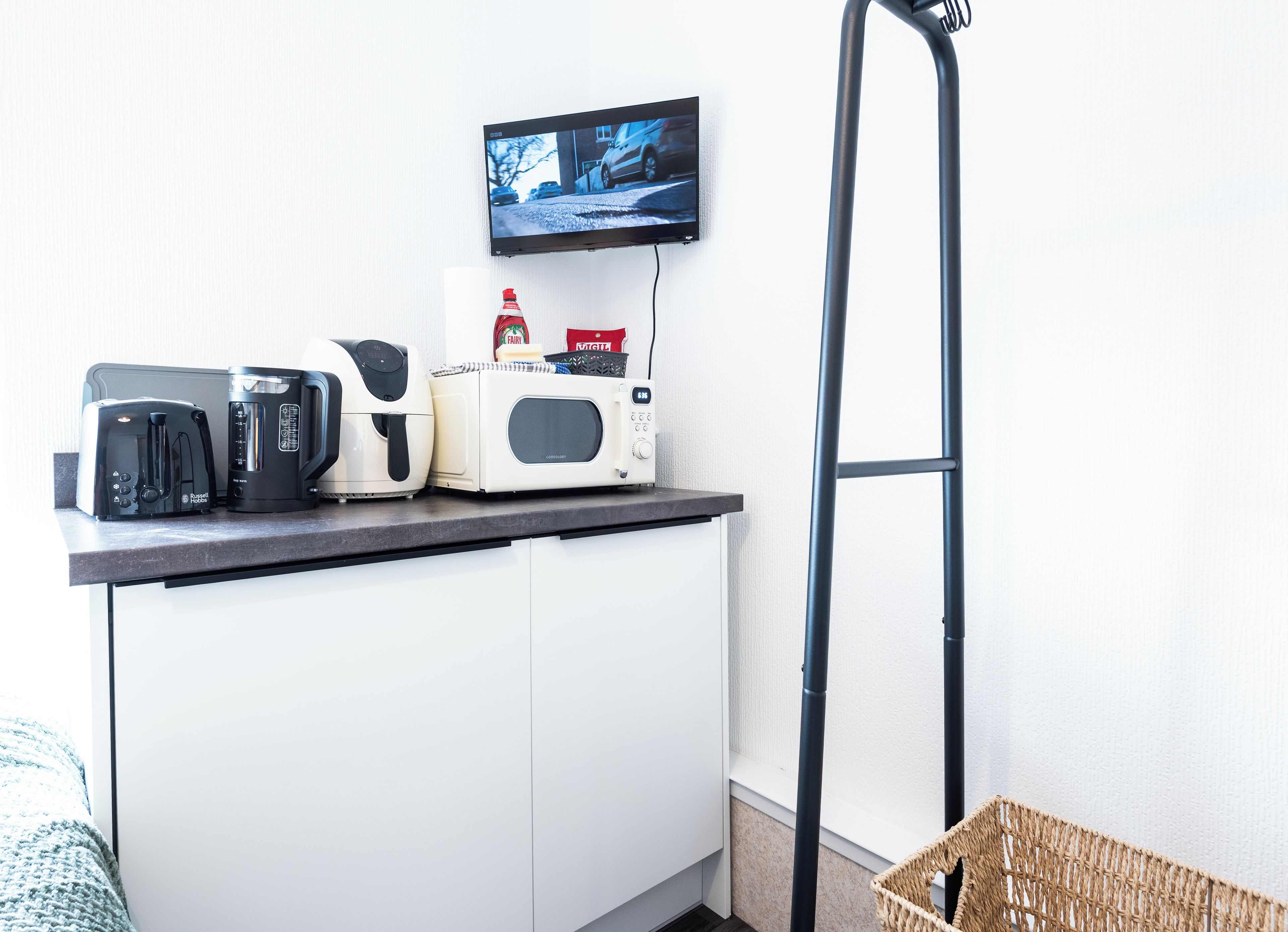 A kitchenette with a toaster, coffee maker, microwave, and a TV mounted on the wall.