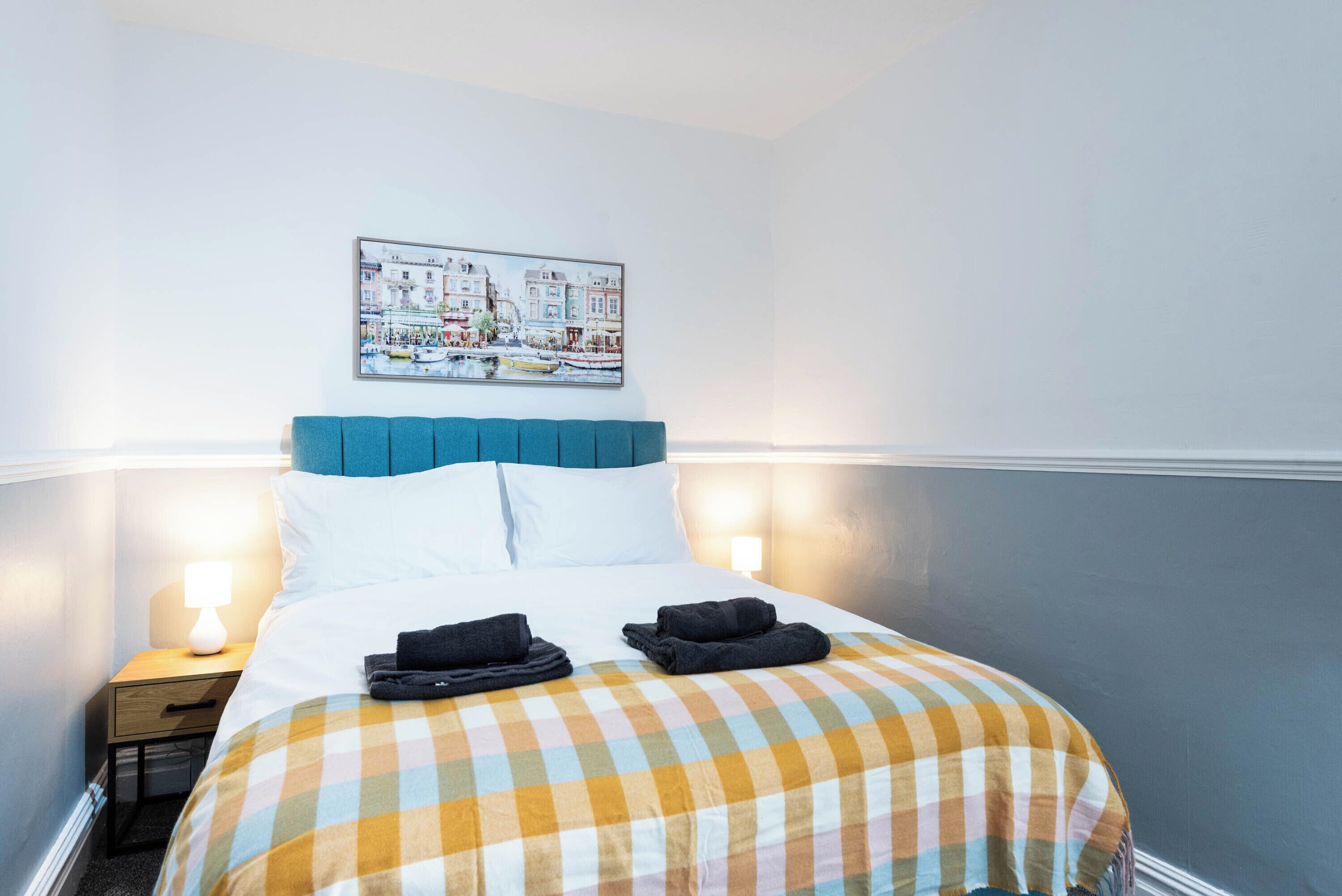 Una habitación de hotel con cama, mesita de noche, lámpara y un cuadro colgado en la pared.
