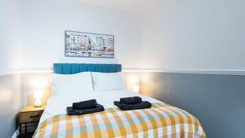 Una habitación de hotel con cama, mesita de noche, lámpara y un cuadro colgado en la pared.