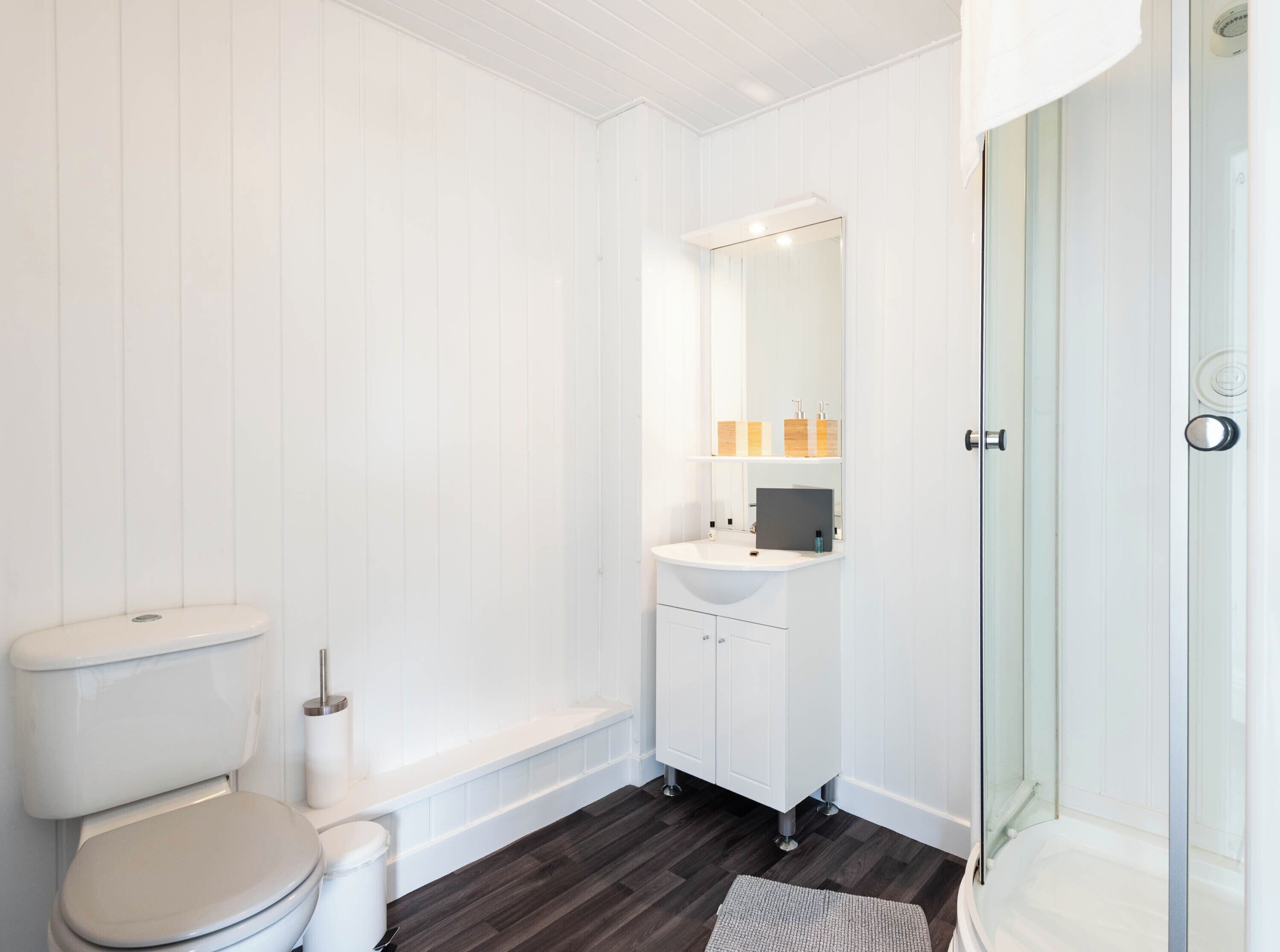Casa de banho com sanita, lavatório, espelho e zona de duche.