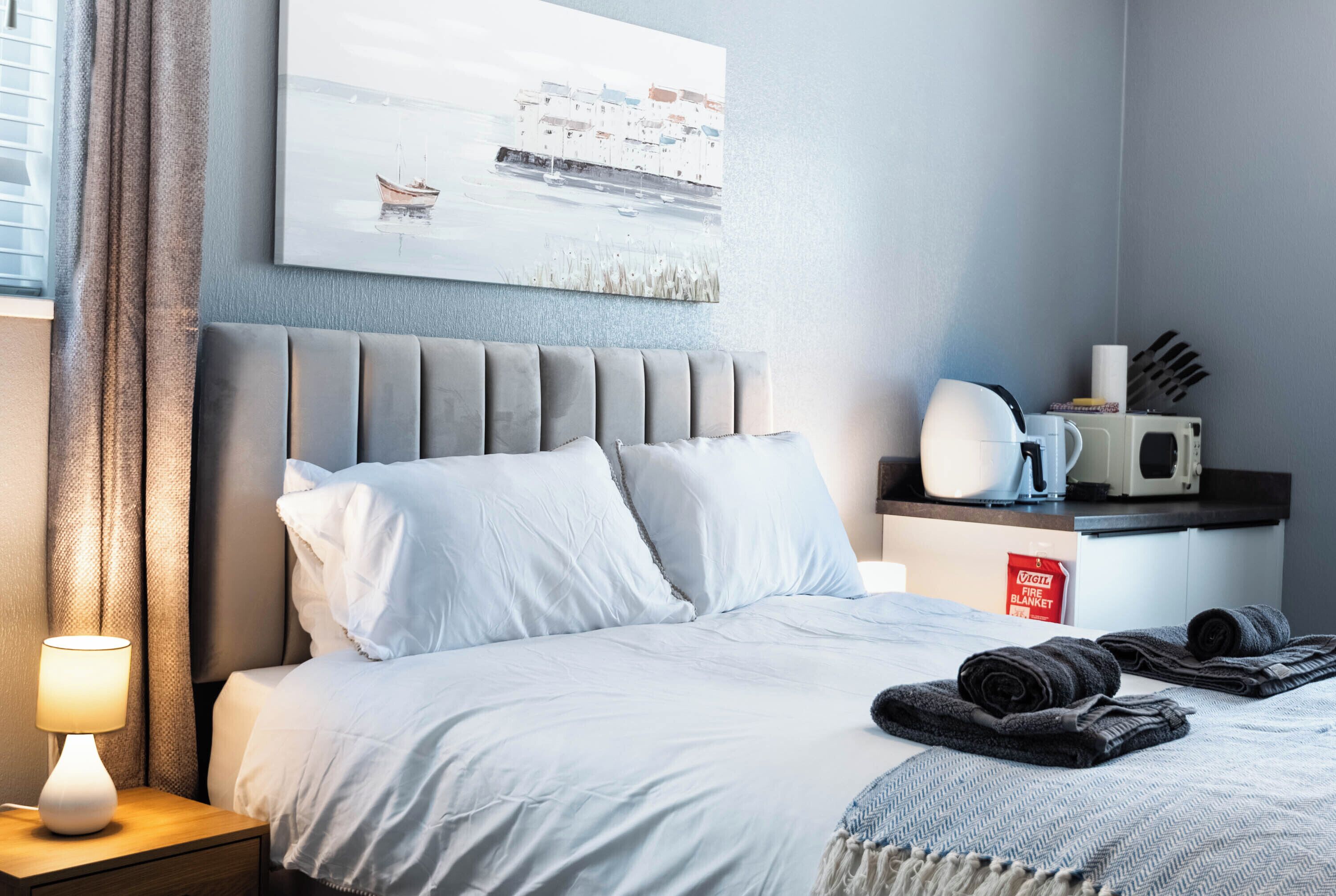 A hotel room with a bed, a nightstand with a lamp, a painting on the wall, a microwave, and a coffee maker.