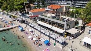 Eine Luftaufnahme einer Küstenregion mit Strand, einem Restaurant mit Außenbereich und einem modernen Gebäude mit rotem Dach.