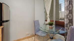 A balcony with a glass table, a chair, a potted plant, and a window with curtains. - Studio w/Kitchenette, AC, WiFi, & Flat Screen - Waikīkī Grand #400 (Honolulu)