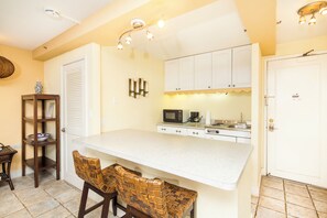 A compact kitchen with a white countertop, a microwave, a coffee maker, and a small dining area with two wicker chairs. - City View Studio w/Kitchenette - Waikīkī Grand 722 (Honolulu)