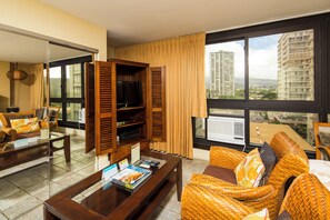 A hotel room with a large window, a television, wicker furniture, and a coffee table. - City View Studio w/Kitchenette - Waikīkī Grand 722 (Honolulu)