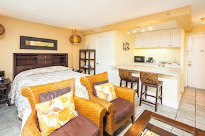 A bedroom with a bed, two wicker chairs, a small kitchenette, and a bathroom. - City View Studio w/Kitchenette - Waikīkī Grand 722 (Honolulu)